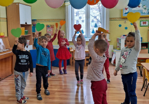 Podczas zabawy ruchowej dziecko zatrzymuje się obok tej osoby, która trzyma serduszko w takim samym kolorze. Nad głowami dzieci wiszą kolorowe balony.